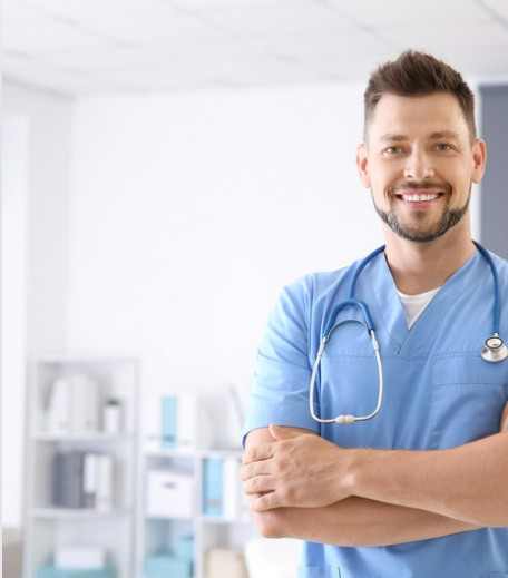 A smiling nurse in blue scrubs with a stethoscope, arms folded